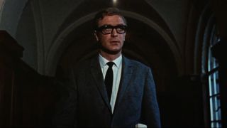 Michael Caine walking down a hallway in his trademark suit and glasses in The Ipcress File.