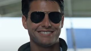 Tom Cruise grins as he wears his aviators in the hangar in Top Gun.